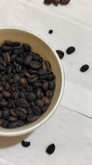 A bowl of freshly roasted coffee beans is dark in color, on a white background.