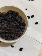 A bowl of freshly roasted coffee beans is dark in color, on a white background.