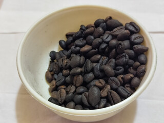 A bowl of freshly roasted coffee beans is dark in color, on a white background.