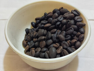 A bowl of freshly roasted coffee beans is dark in color, on a white background.
