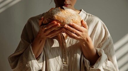 A young Asian woman holds a freshly baked loaf of bread in her hands. She wears a light-colored, loose-fitting shirt. Soft light creates gentle shadows. - Powered by Adobe