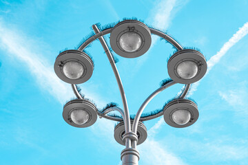 A modern street lamp with six lights against a bright blue sky.
