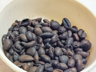 A bowl of freshly roasted coffee beans is dark in color, on a white background.