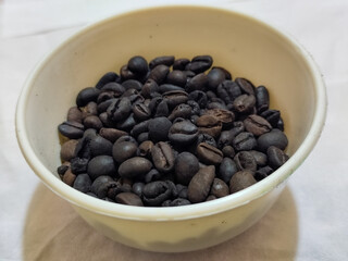 A bowl of freshly roasted coffee beans is dark in color, on a white background.