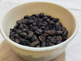 A bowl of freshly roasted coffee beans is dark in color, on a white background.