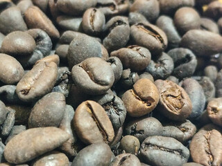 Dense clusters of dark roasted coffee beans, revealing a deep brown color, fill the frame in the...
