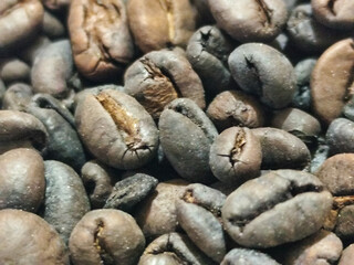 Dense clusters of dark roasted coffee beans, revealing a deep brown color, fill the frame in the...