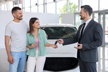 Smiling salesman giving car key to happy family in salon