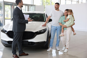 Salesman with clipboard showing new car to happy family in salon