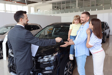 Salesman giving car key to happy family in salon