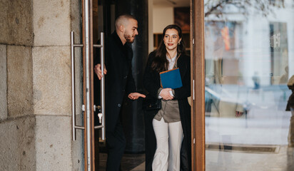 Two business individuals leaving a commercial building, reflecting professionalism and purposeful...