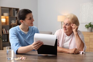 Nurse with clipboard examining senior woman at wooden table indoors. Home health care service
