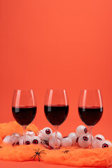 Red wine glasses with spooky eyeball lights and black spiders on orange Halloween-themed background with festive setup.