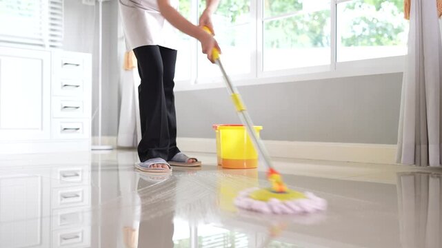 The housekeeper continuously cleans the floor with a mop in the long living room of the house to keep the house clean.