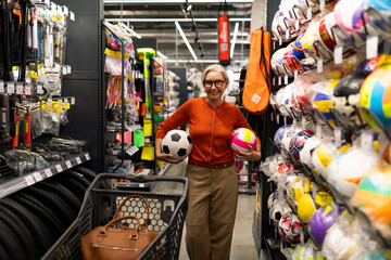 Middle-aged woman shops for sports equipment in a large retail store, enjoying her shopping...