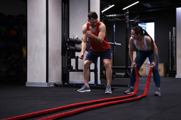 Young woman exercising with battle ropes and professional personal trainer in gym