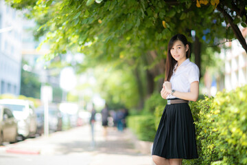 A cute Asian student poses for a photo at her university's faculty, trying to balance her student...