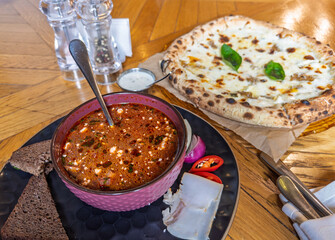 Hearty red borscht in a textured bowl with dark rye bread and sliced salo next to cheesy Italian pizza slice
