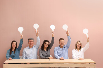 Panel of happy judges voting with blank score signs at tables against beige background