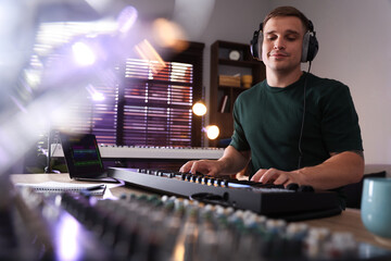 Man in headphones working with MIDI keyboard at table in home studio, low angle view
