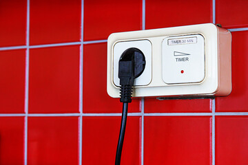 A closeup of a black electrical plug inserted into a beige timer switch outlet mounted on a red...