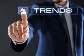 Businessman using virtual screen to find hot tendencies, new ideas, popular directions against grey background, closeup. Search bar with word Trends