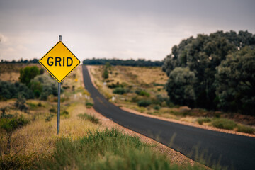 A yellow diamond-shaped road sign with the word “GRID” placed on the left side of a two-lane road
