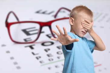 Little boy with eyesight problems, glasses and vision test chart