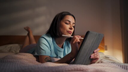 A young woman creates digital art on her tablet in her cozy bedroom at night - Powered by Adobe