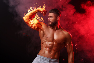 Bodybuilder showing his biceps in smoke against dark background. Muscular man with flaming arm