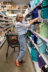 Woman shopping in a hypermarket while selecting colorful storage containers for home organization...