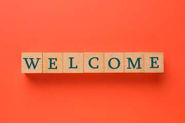 Word Welcome made of wooden cubes on red background, top view