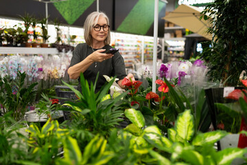 Middle-aged woman exploring a large store's garden section, selecting plants and engaging with...