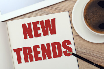 New Trends inscription in notebook, coffee and pen on wooden table, top view