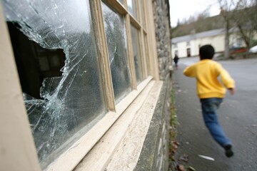 Childhood vandalism, an unrecognizable boy flees down the street after smashing a window with a stone