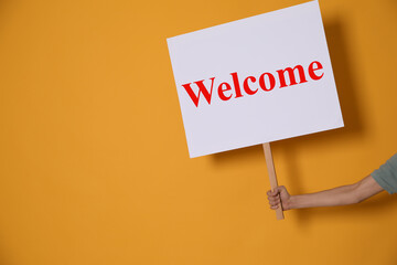 Woman holding Welcome sign on orange background, closeup