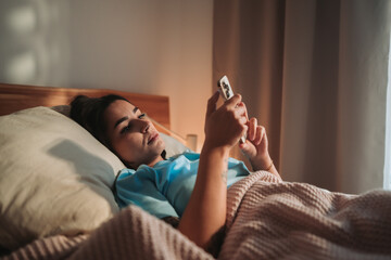 Young Woman Relaxing in Bed While Using Smartphone for Leisure Activities