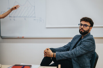 A focused student listens attentively in a classroom while a graph is discussed on the board. The atmosphere is casual, promoting engagement and interactive learning.