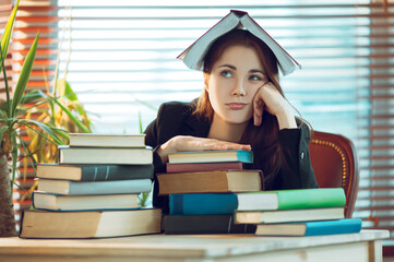 Portrait of beautiful student girl sitting among books with a book on her head