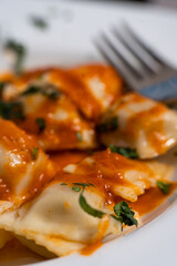 Ravioli pasta with tomato sauce and parsley on white plate with fork: close-up. Vertical Orientation