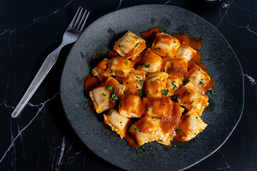 Ravioli pasta with tomato sauce and parsley on dark plate