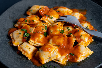 Ravioli pasta with tomato sauce and parsley topping on elegant dark grey plate
