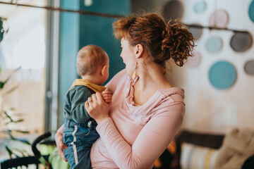 A woman in casual clothing embraces her young child in a colorful interior setting, symbolizing the...
