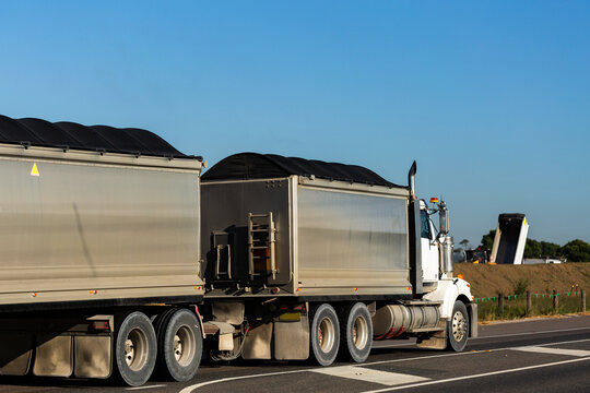 Covered semi-trailer tuck hauling dirt on road passing worksite