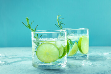 Gin tonic, two glasses of gin with soda, lime, rosemary, and plenty of ice, side view on a blue background, fresh summer cocktails