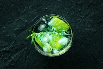Gin tonic, overhead flat lay shot with rosemary and lime. Fresh summer drink with ice, on a black background
