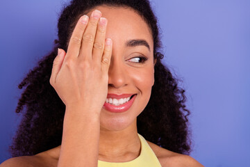 Charming young woman with natural curls posing playfully against a vibrant purple background,...