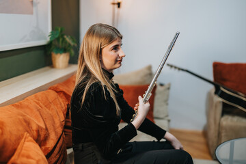 A young woman with long hair is sitting on a sofa holding a flute, with musical instruments and...