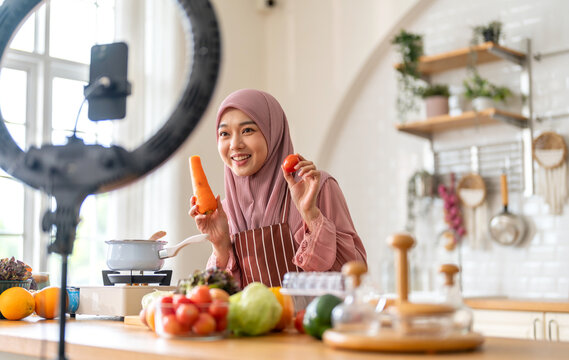 Muslim woman vlogger live streaming cooking online in kitchen look at camera with vegetables, content creator culinary class at home studio, halal food influencer cooking live, video for social media