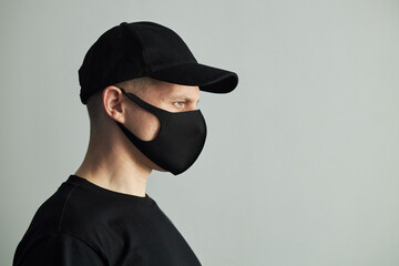 Caucasian young man wearing black cap and face mask standing in profile against plain white...